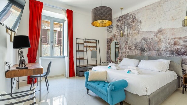 Une chambre à coucher avec un lit, un bureau, une chaise, un canapé bleu, un miroir et une fenêtre avec des rideaux rouges.