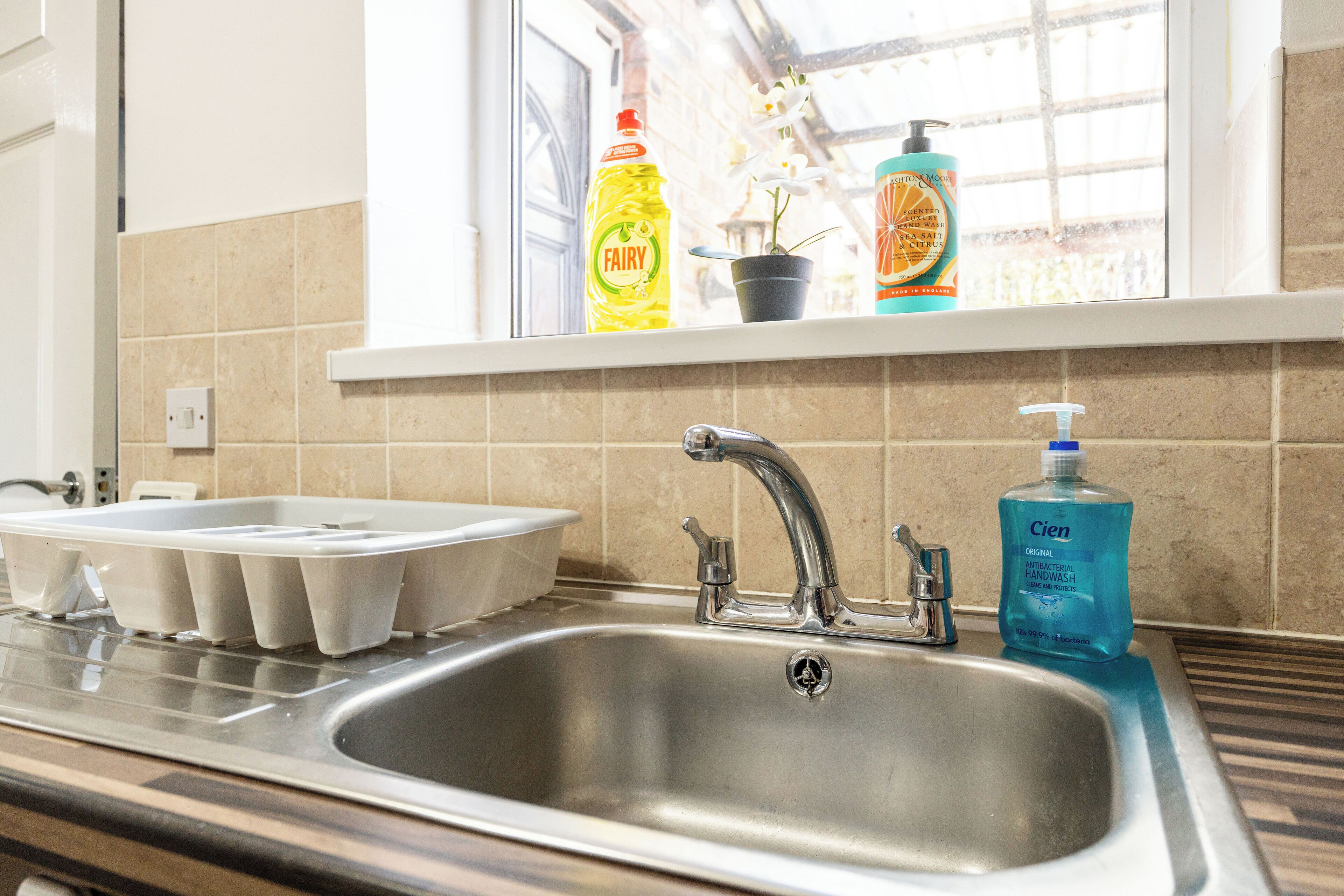 A kitchen with a stainless steel sink, a window with a view, and various toiletries on the windowsill.
