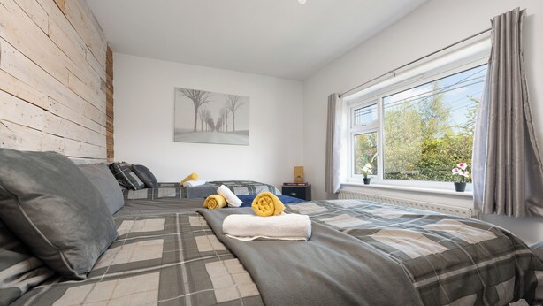 Een slaapkamer met een groot bed, een raam met gordijnen, een nachtkastje en een schilderij aan de muur.