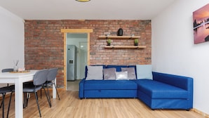 Een woonkamer met een blauwe bank, een houten eettafel met stoelen, een bakstenen muur en een houten vloer.