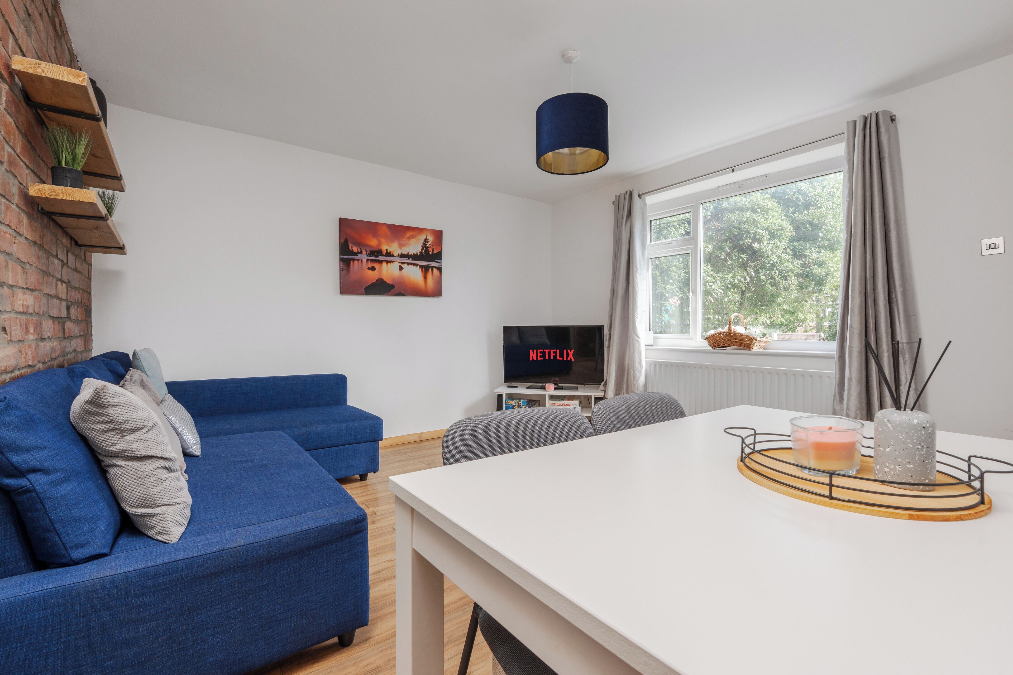 A modern living room with a blue sofa, a white table, and a TV displaying 'NETFLIX'.