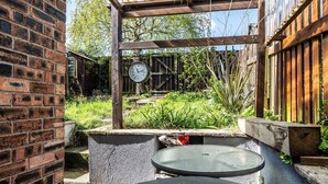 Een terras met een bakstenen muur, een houten pergola en een ronde tafel.