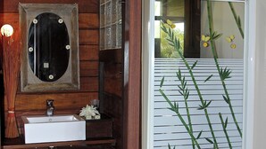 A bathroom with a wooden interior, a white sink, a mirror, and a glass shower door with bamboo decoration.