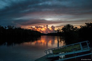 A sunset over a calm river with a dock and a signboard.