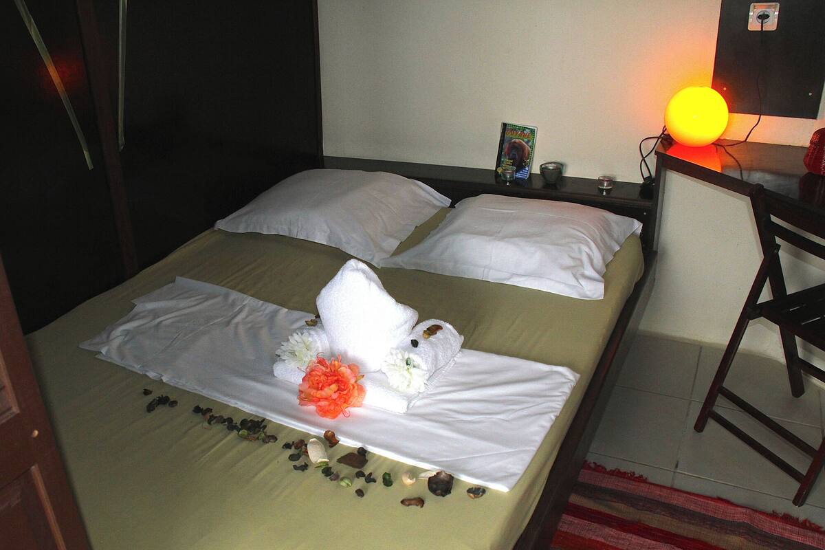 Un lit bien fait, avec des draps blancs, une serviette et des pétales de rose éparpillés.