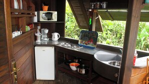A compact kitchen with wooden walls, a white refrigerator, a microwave, a gas stove, and a sink.