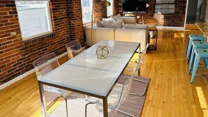 A modern living room with a glass dining table, clear chairs, a sofa, and a TV. - Spacious and luxurious downtown loft in Logansport w/ incredible rooftop patio (Logansport)