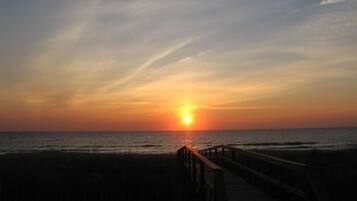 A sunset over the ocean with a wooden pier leading to the beach.