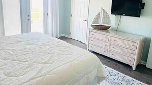Een slaapkamer met een bed, een dressoir, een televisie en een deur.
