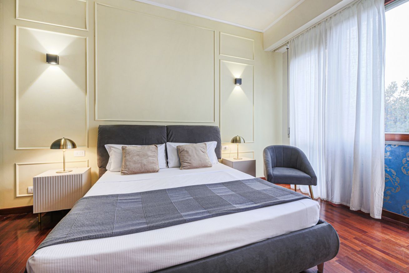 Habitación de hotel con una cama grande, lámparas de noche, una silla y vistas al exterior.