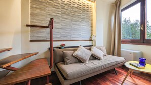 Une pièce comprenant un canapé, des tables en bois, une fenêtre avec des rideaux et un mur orné d’un motif texturé.