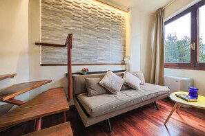 Une pièce comprenant un canapé, des tables en bois, une fenêtre avec des rideaux et un mur orné d’un motif texturé.