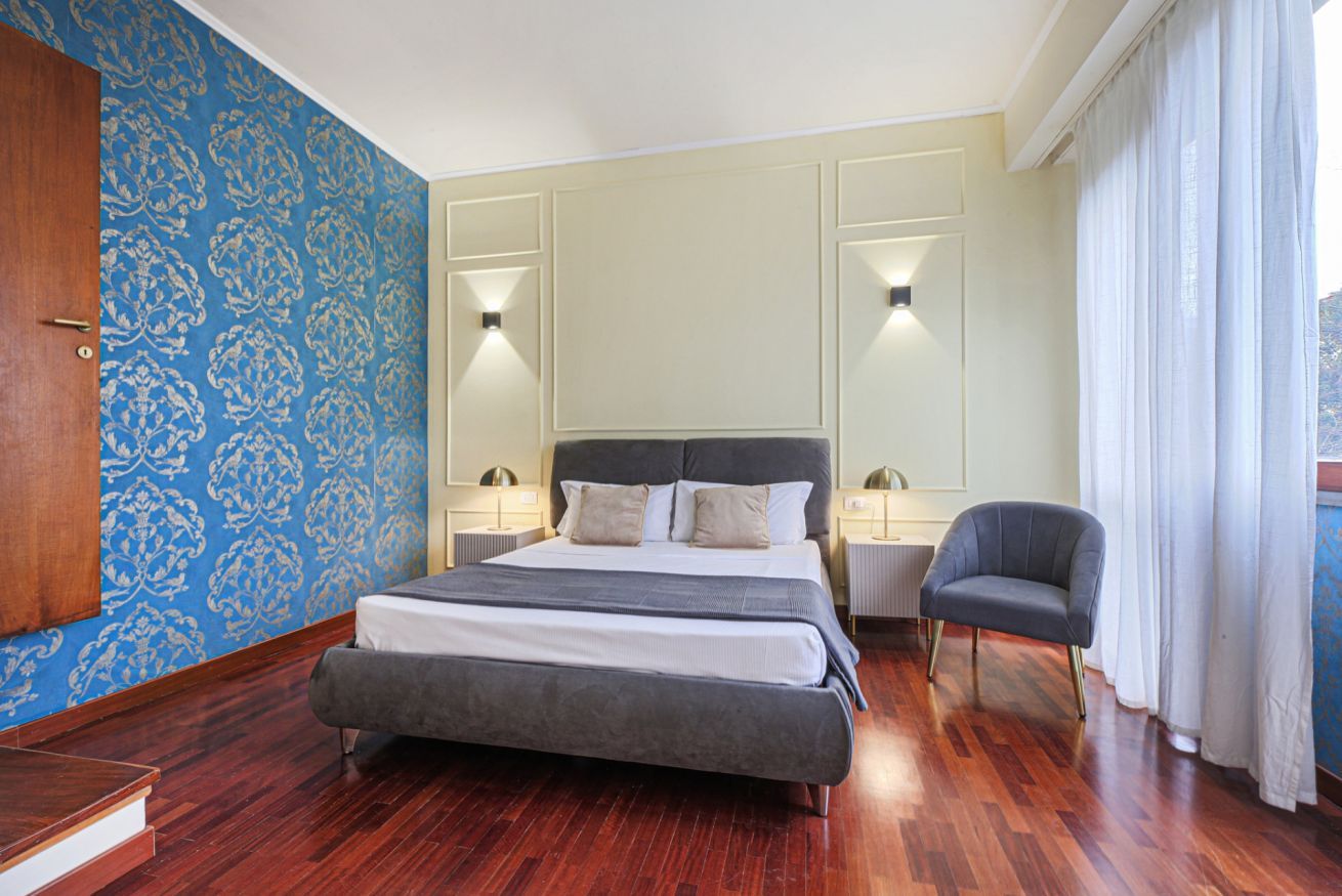 Quarto com uma cama grande, mesas de cabeceira, uma cadeira e parede estampada.