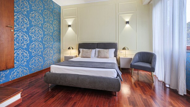 Une chambre avec un grand lit, des tables de chevet, une chaise et un mur décoré d’un motif.