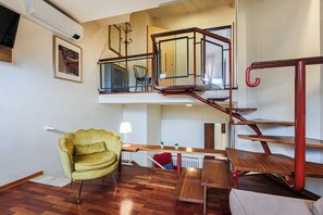 Ett bostadsutrymme med flera nivåer, en trappa, en gul fåtölj, ett träbord och ett element.