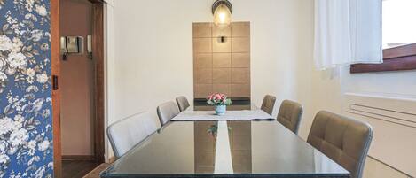 Un coin repas comprenant une table en verre, six chaises, un vase avec des fleurs, un luminaire fixé au mur et une porte en bois.
