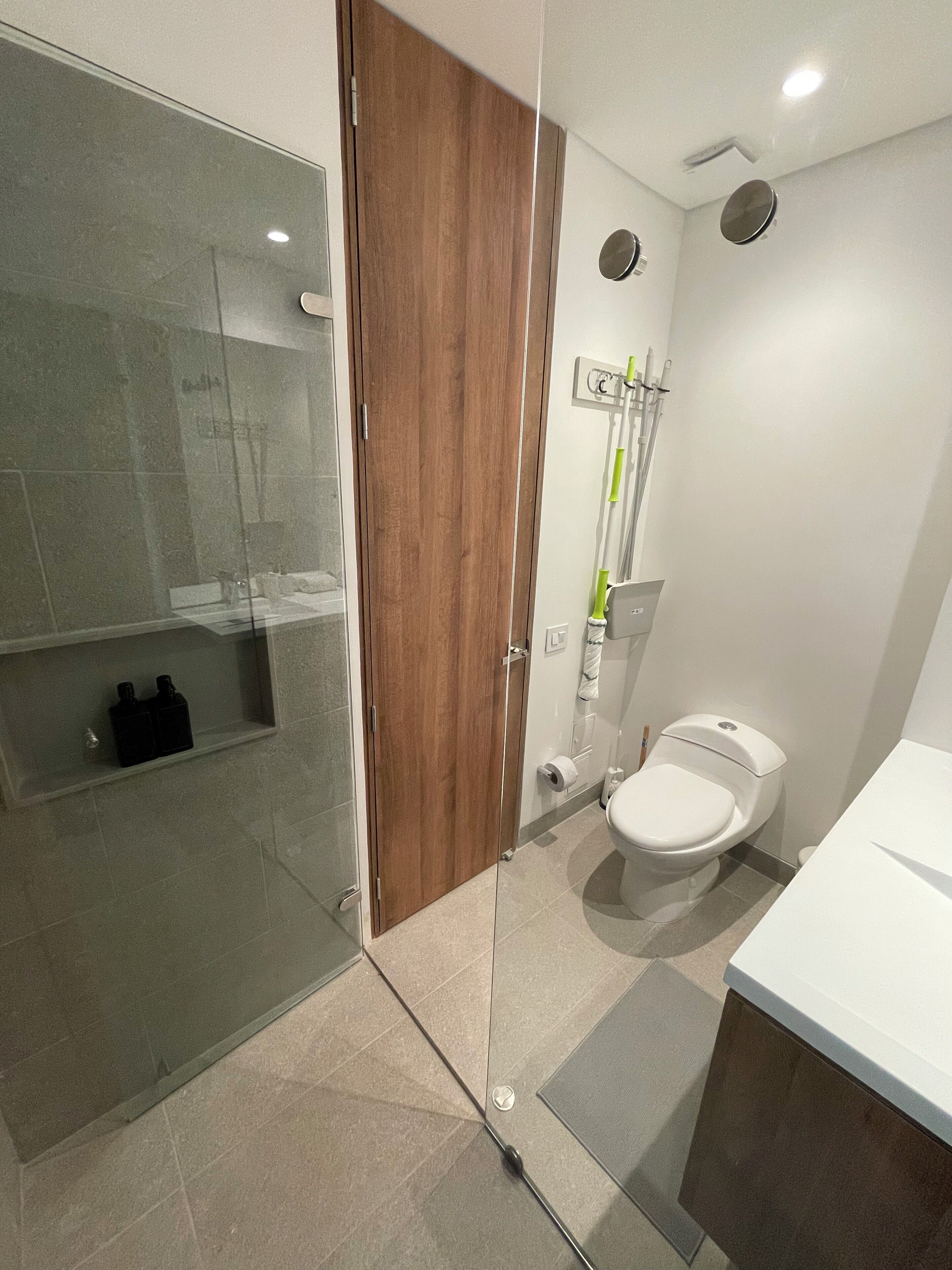 Un baño moderno con cabina de ducha de vidrio, puerta de madera, inodoro y lavabo blanco.