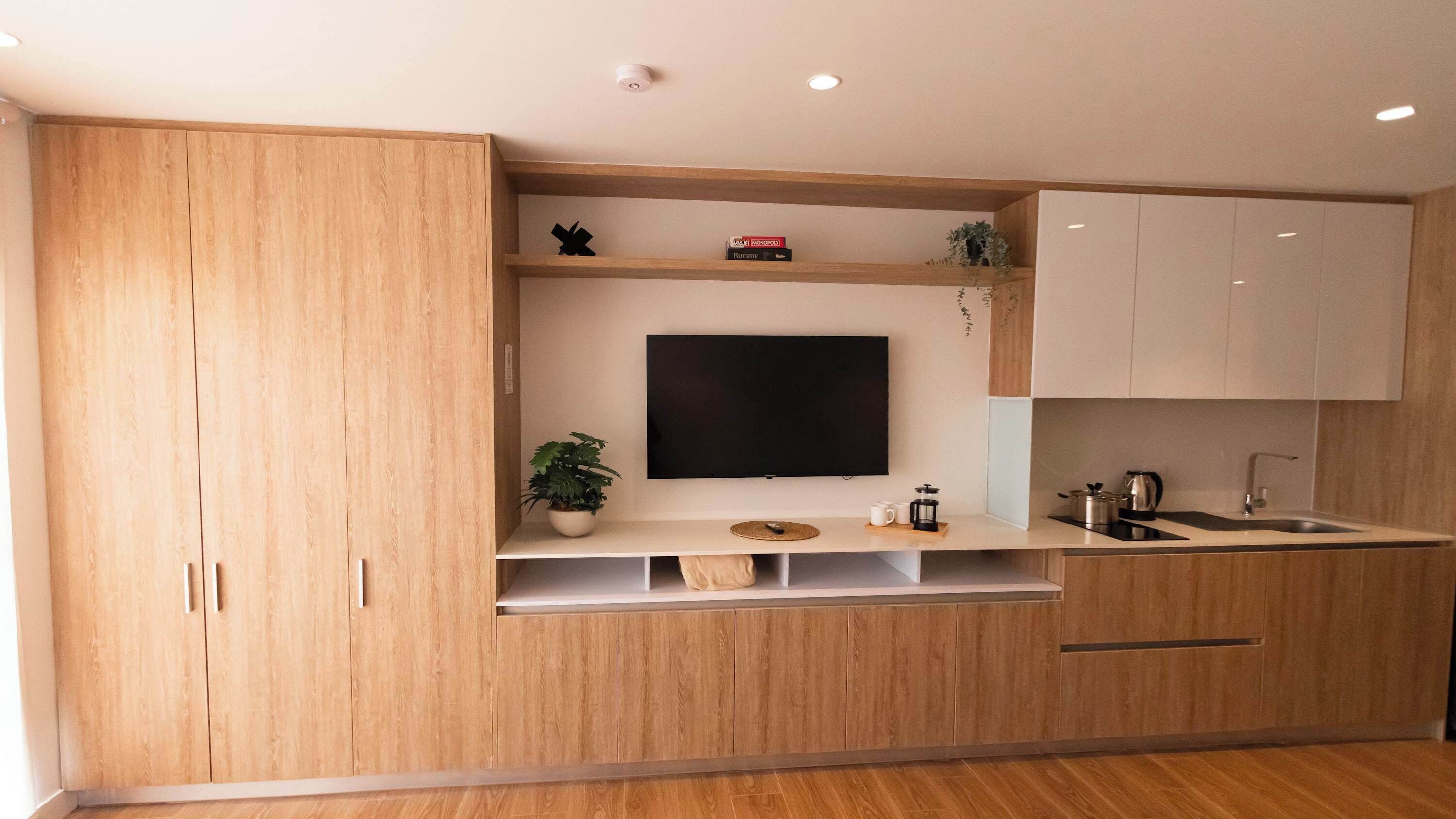 A modern kitchen with wooden cabinets, a built-in TV, and a sink.