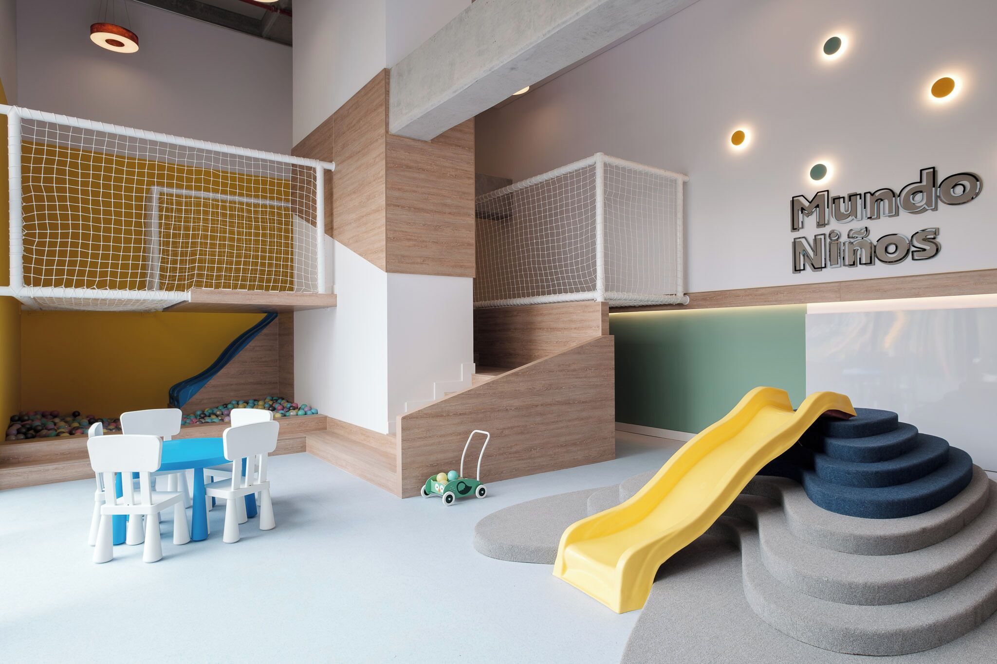 Zona de juegos infantiles con tobogán, red de escalada y una mesa con sillas.