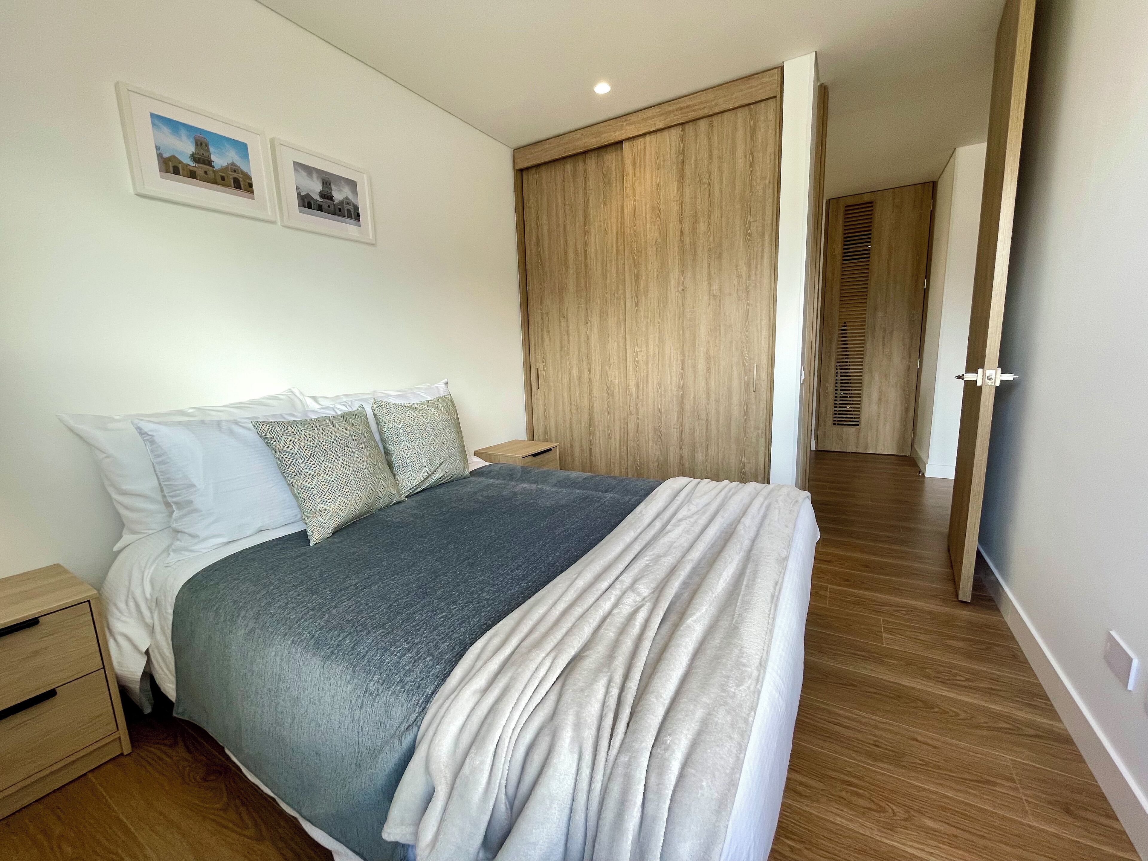 A bedroom with a bed, nightstands, a wooden wardrobe, and two framed pictures on the wall.