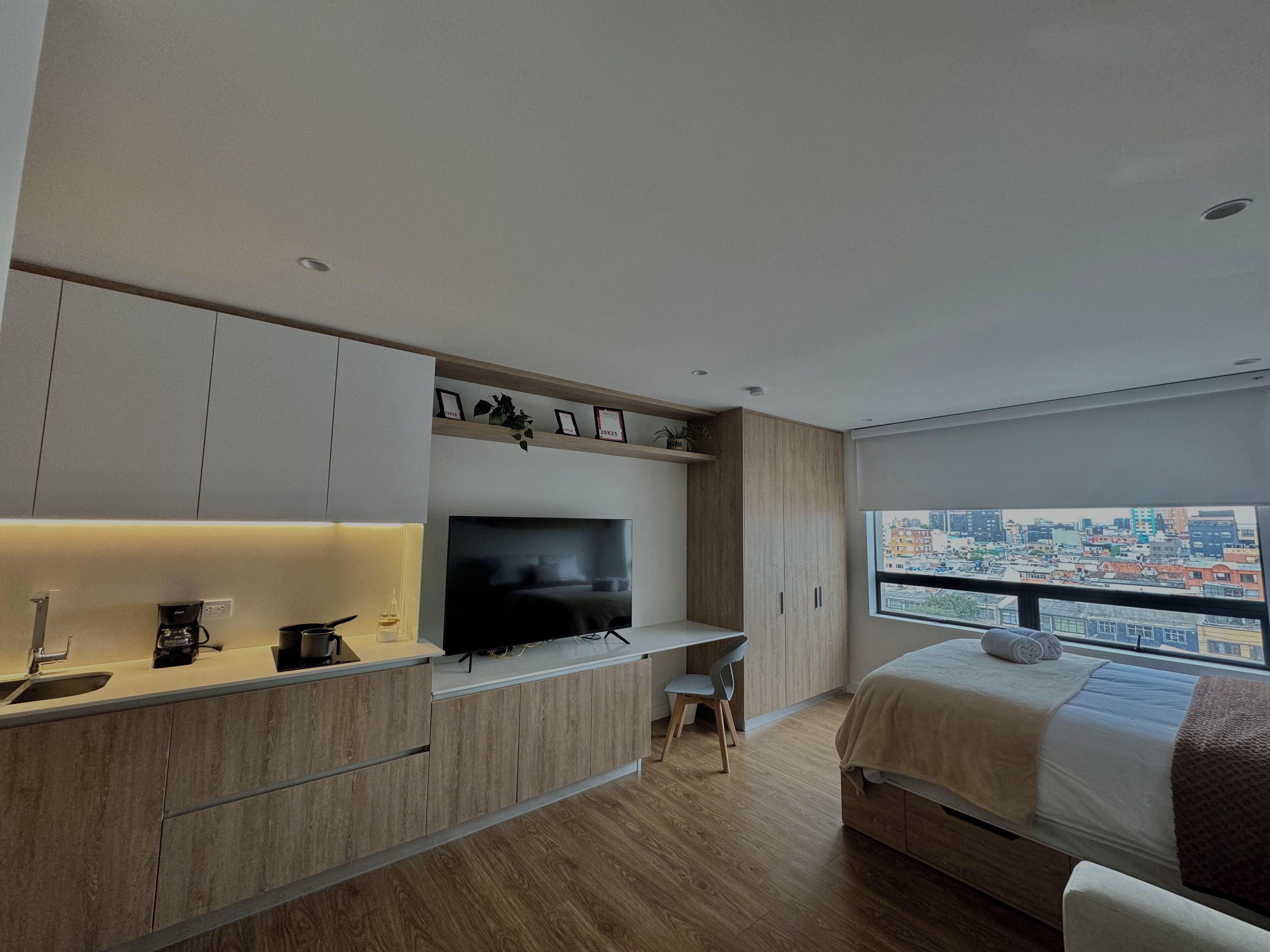 Ein modernes Schlafzimmer mit einem großen Bett, einem Fernseher, einem Schreibtisch und Blick auf die Stadt.