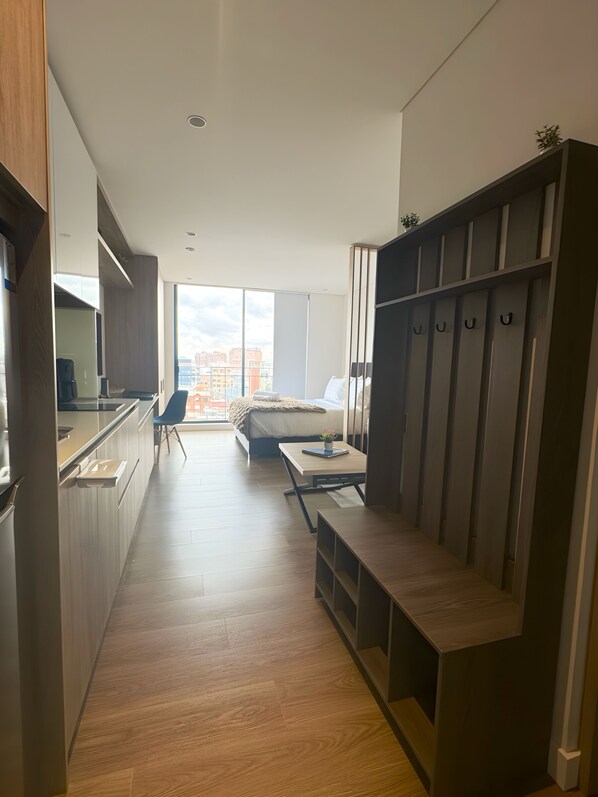 A modern hotel room with a kitchenette, a bed with a city view, a seating area, and a wardrobe with hooks. - Avanzza by Wellcome (Bogotá)