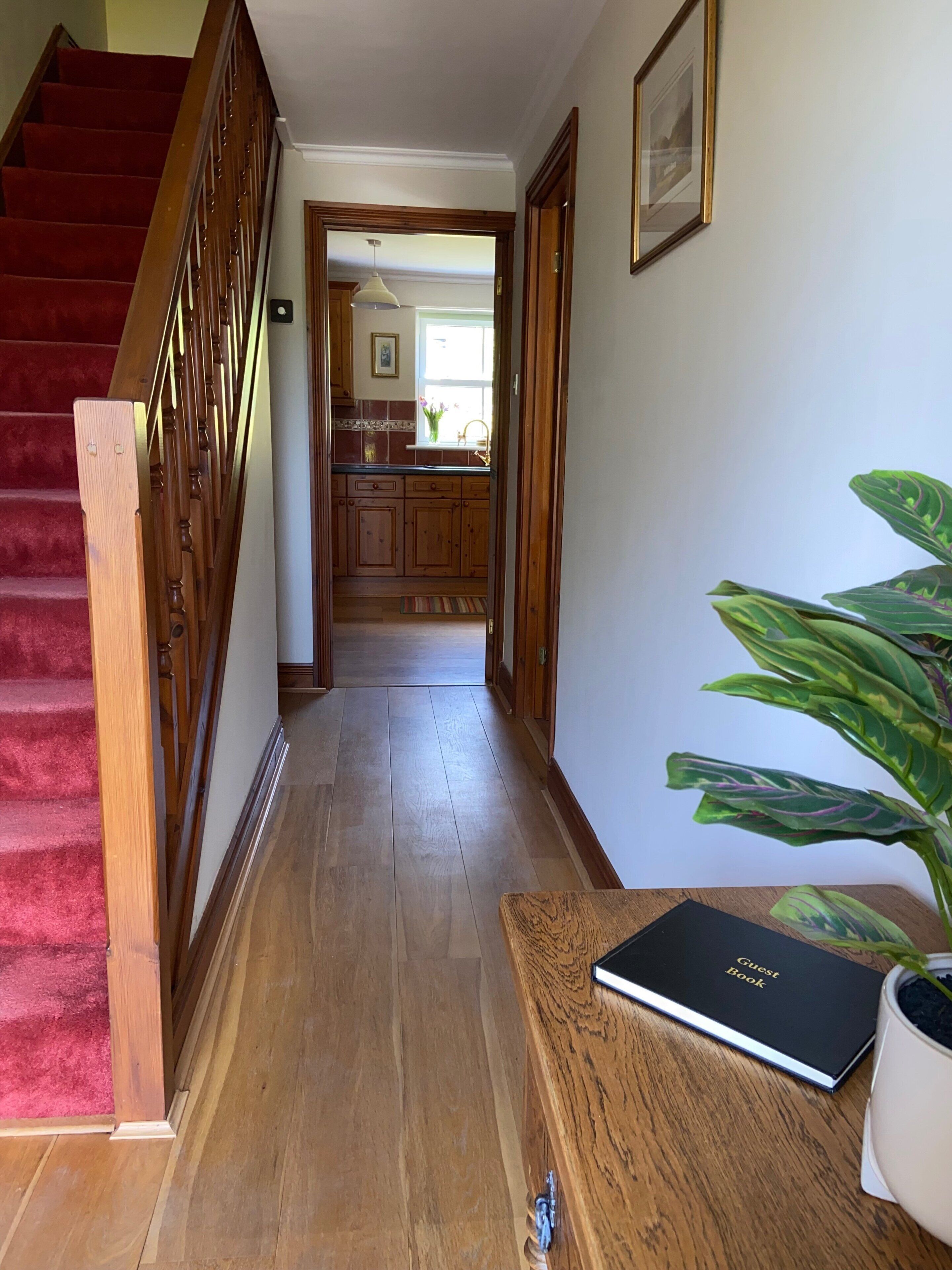 Un escalier en bois mène à une cuisine dotée de meubles de rangement en bois et d’une fenêtre.