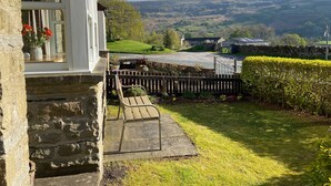 A stone house with a wooden bench and a gate leading to a green field.