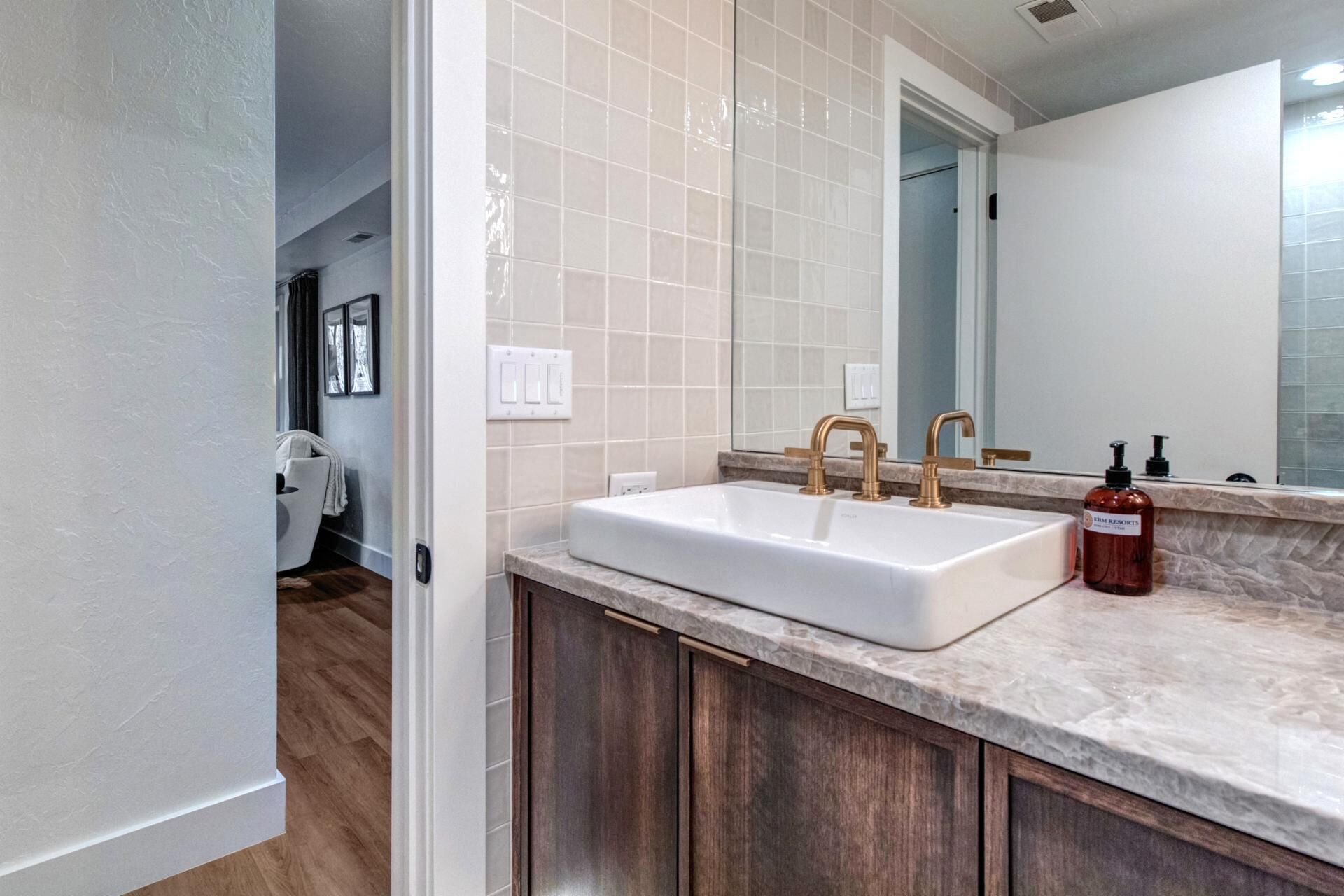 A bathroom with a white sink, wooden cabinets, and a marble countertop.