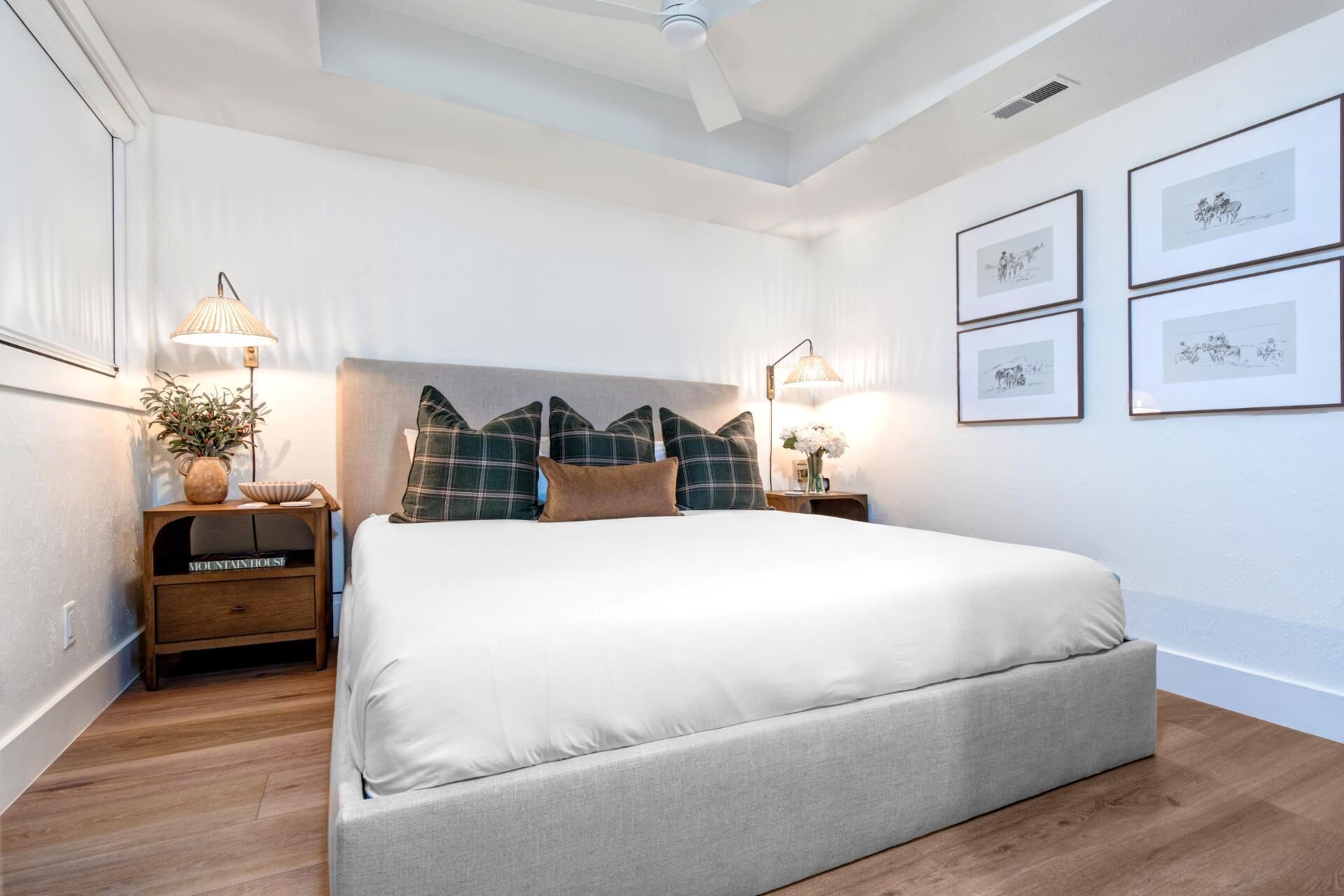 Un dormitorio ordenado con una cama grande, mesitas de noche con lámparas y cuadros en la pared.