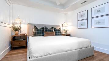 Un dormitorio ordenado con una cama grande, mesitas de noche con lámparas y cuadros en la pared.