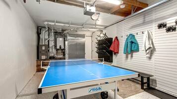 A ping pong table in a room with a white wall and a wooden ceiling. There are jackets hanging on the wall.