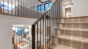 A staircase with a woven carpet and black metal railings, leading to a room with a view of the outdoors.