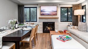 A modern living room with a fireplace, dining area, and a sofa with a game box.