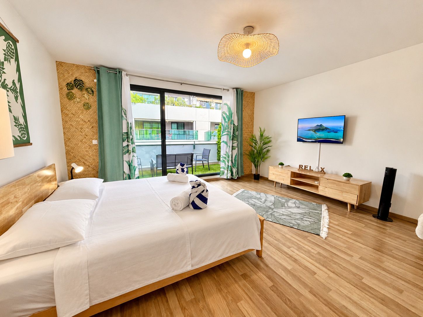 A hotel room with a bed, a TV, a wooden dresser, and a balcony with a view.