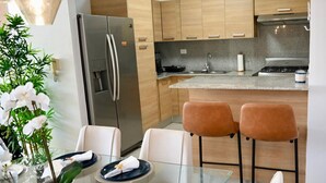Une cuisine moderne dotée d’un réfrigérateur en acier inoxydable, de meubles en bois, d’un plan de travail en granit et de deux tabourets de bar.