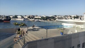 Vue d’une zone riveraine avec une piscine, des chaises longues et un grand navire amarré au loin.