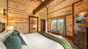 Een slaapkamer in een houten chalet, met een bed, een bankje, een dressoir en een televisie.