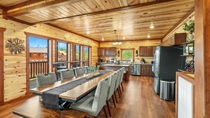 Een ruime houten chalet met een grote eettafel, keuken en grote ramen met uitzicht op het omliggende landschap.