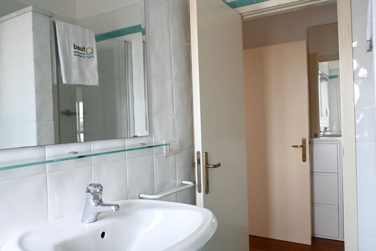 A bathroom with a white sink, a glass shelf, a towel hanging on the wall, and a door leading to another room.