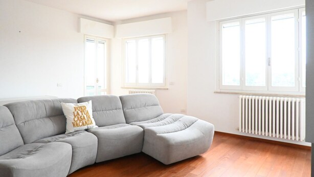 A modern living room with a grey sectional sofa, a radiator, and large windows allowing natural light. - N297 - Numana, three-room apartment in the heart of the town (Numana)