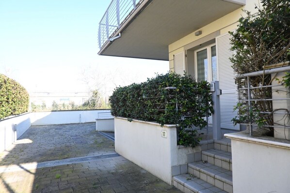 A residential building with a paved patio, a small staircase, and a hedge.