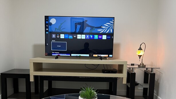 A modern living room with a flat-screen TV on a wooden stand, a glass dining table with a potted plant, and a decorative lamp. - Cozy & Modern 3BR Lower Unit I Private Entrance, Laundry, Fridge Microwave (Calgary)