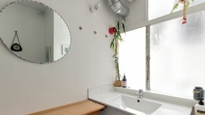 Een badkamer met een ronde spiegel, een wastafel, een raam en een plant.