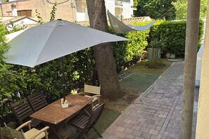 An outdoor patio with a wooden table and chairs, a white umbrella, and a brick pathway.
