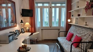 Ein modernes Wohnzimmer mit einer Couch, einem Esstisch, einem Fernseher und einem Fenster mit Vorhängen.