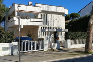 A modern two-story building with a white facade, a gated entrance, and a parked car.