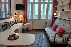 A modern living room with a sofa, a dining table, a TV mounted on the wall, and a window with curtains. - CN008 - Cesenatico, new two-room apartment 30m from the canal (Cesenatico)