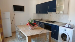 A compact kitchen with a dining table, chairs, a washing machine, and a TV mounted on the wall. - CV004 - Cervia, new three-room apartment with air conditioning (Cervia)