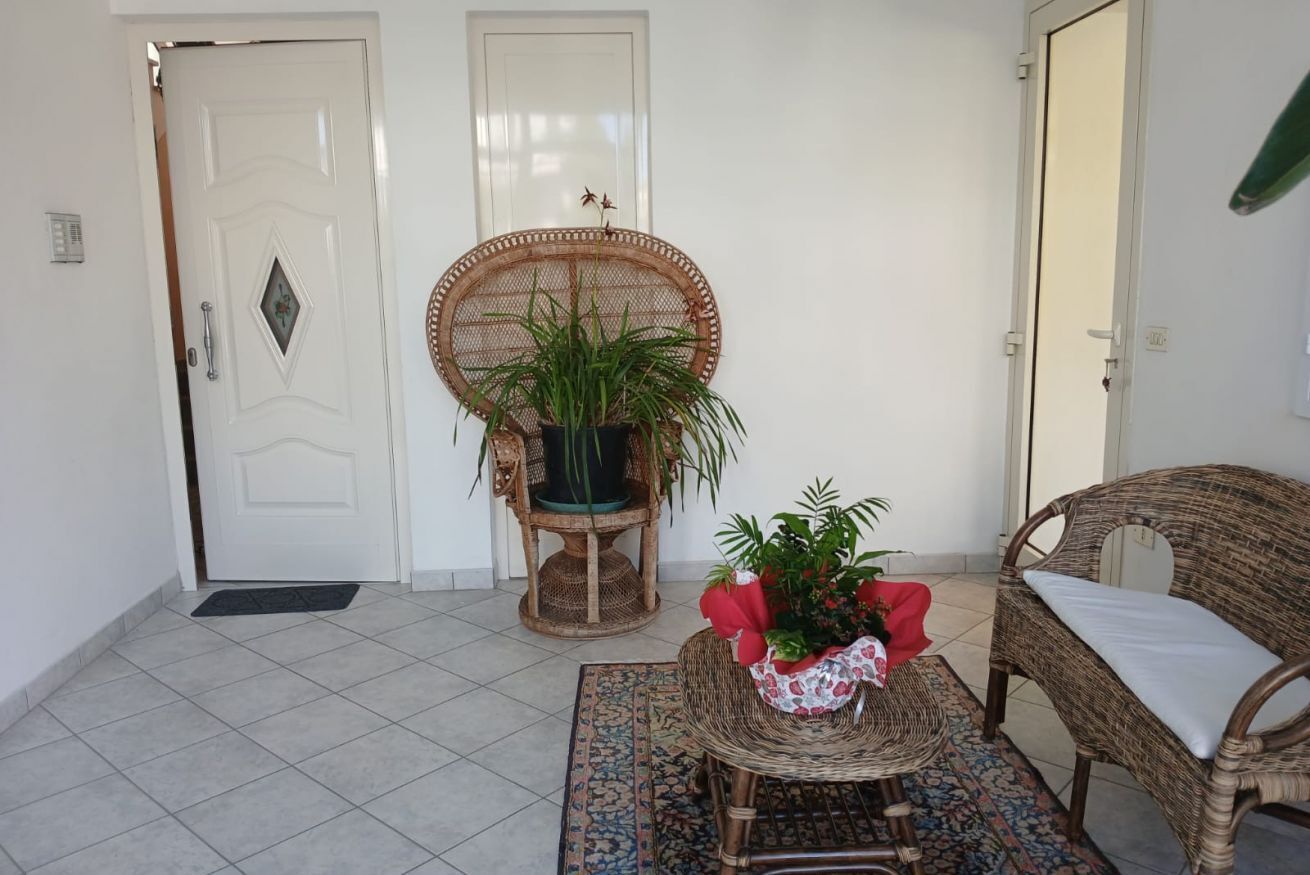 Een kamer met een deur, een rieten stoel met een plant, een rieten tafeltje met een plant, en een rieten bank.